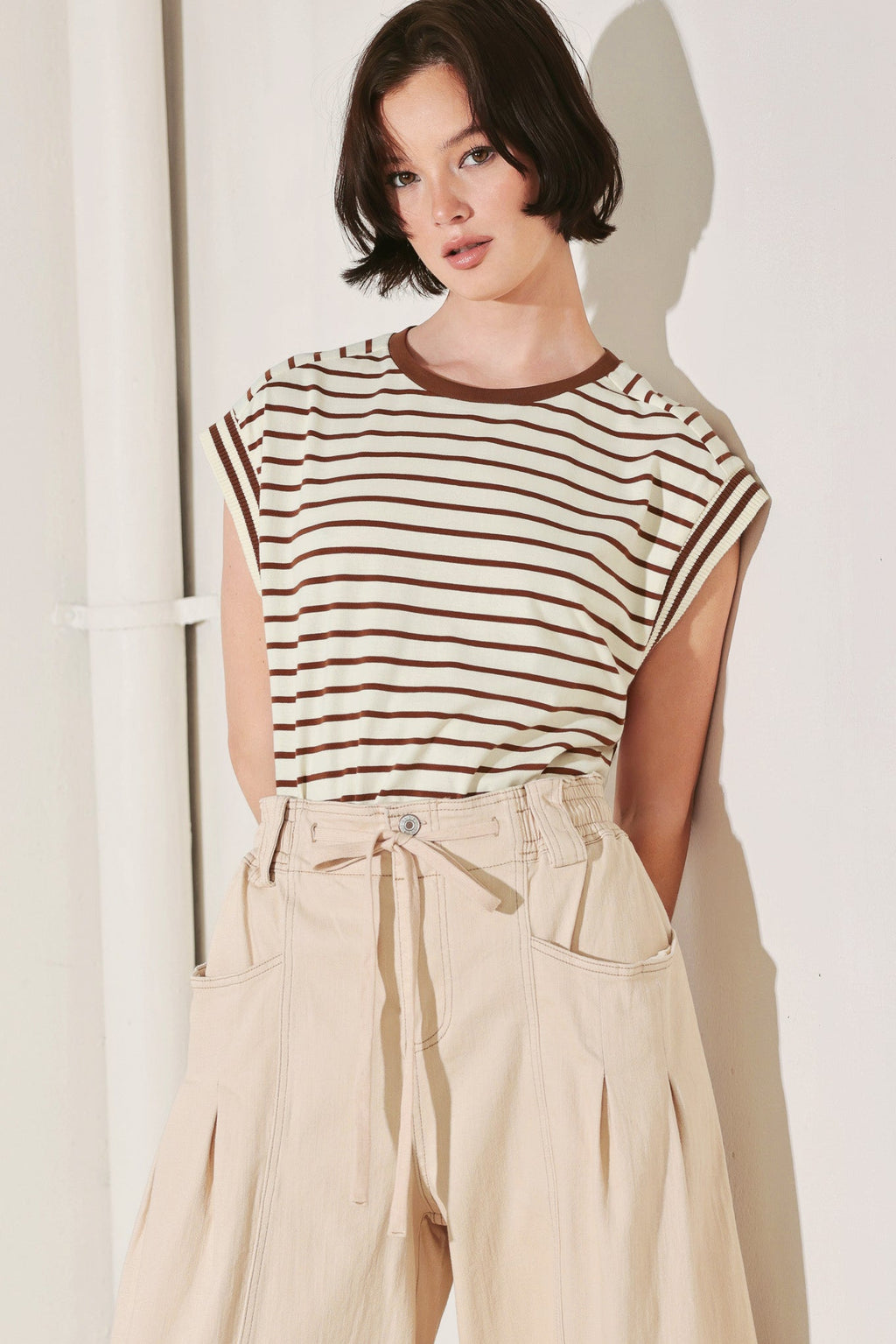 Woman wearing a striped shirt and beige pants against a white background