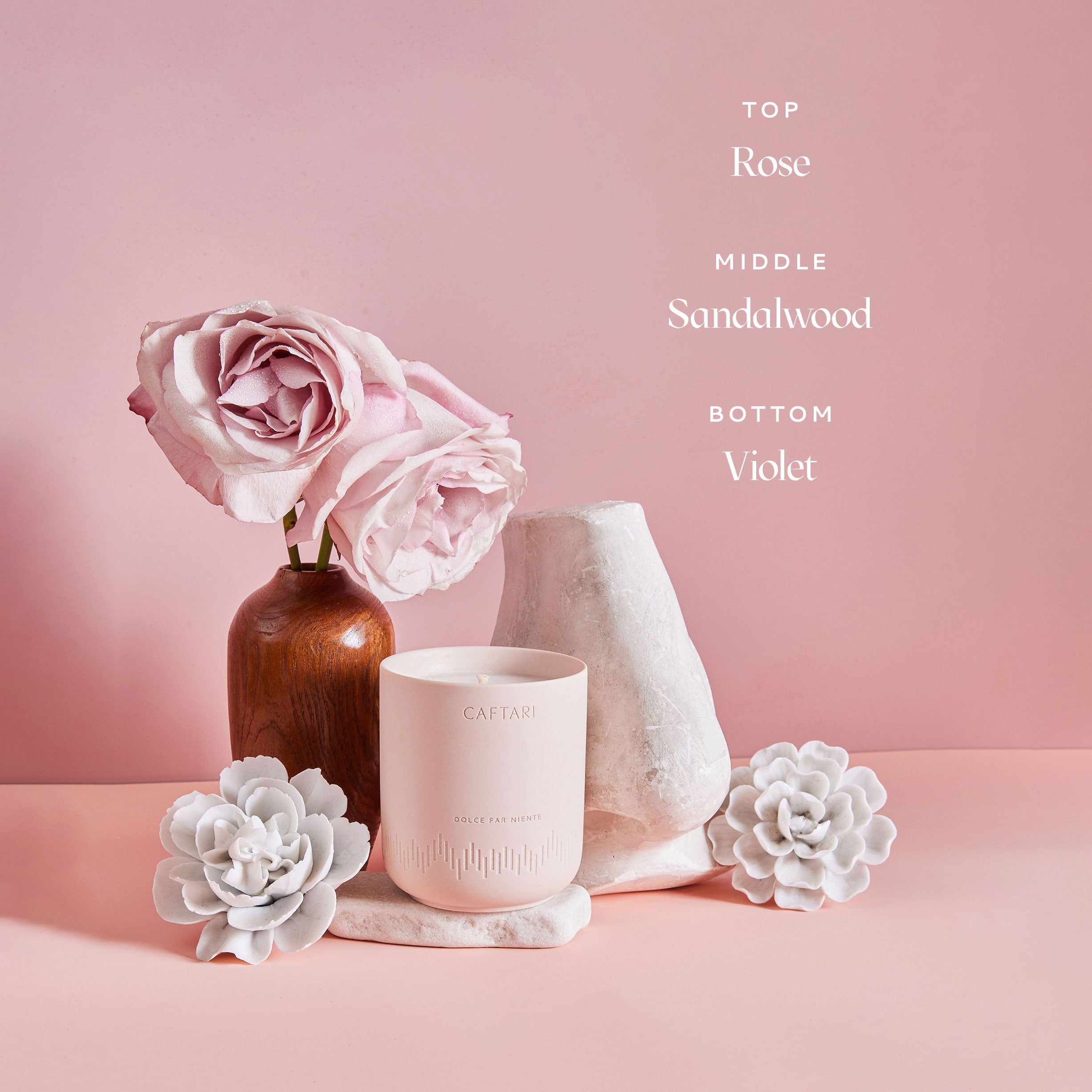 Caftari Dolce Far Niente rose candle with sandalwood and violet fragrance notes in a soft pink floral setting