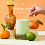Caftari Elixir bergamot essential oil candle surrounded by citrus fruits and lit with a match for uplifting energy