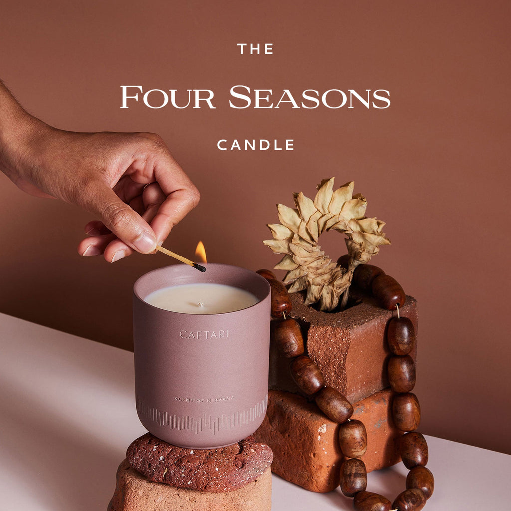 Caftari Scent of Nirvana meditation candle infused with agarwood oud being lit with a match in a warm earth-toned setting