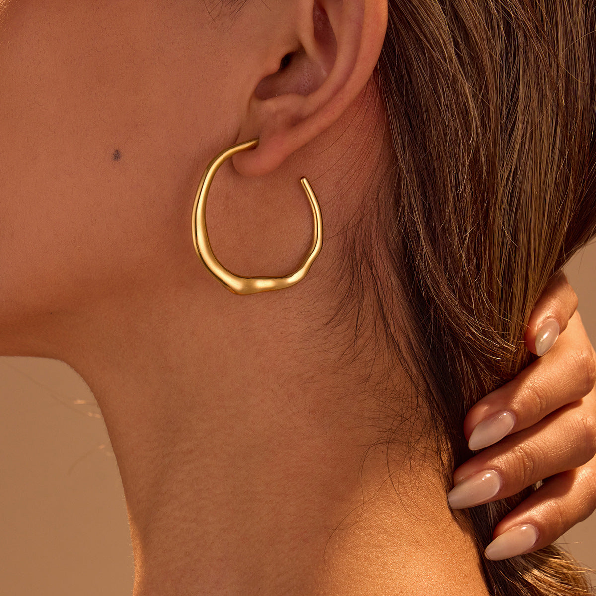 Gold hoop earring worn by a person with a neutral background Main image