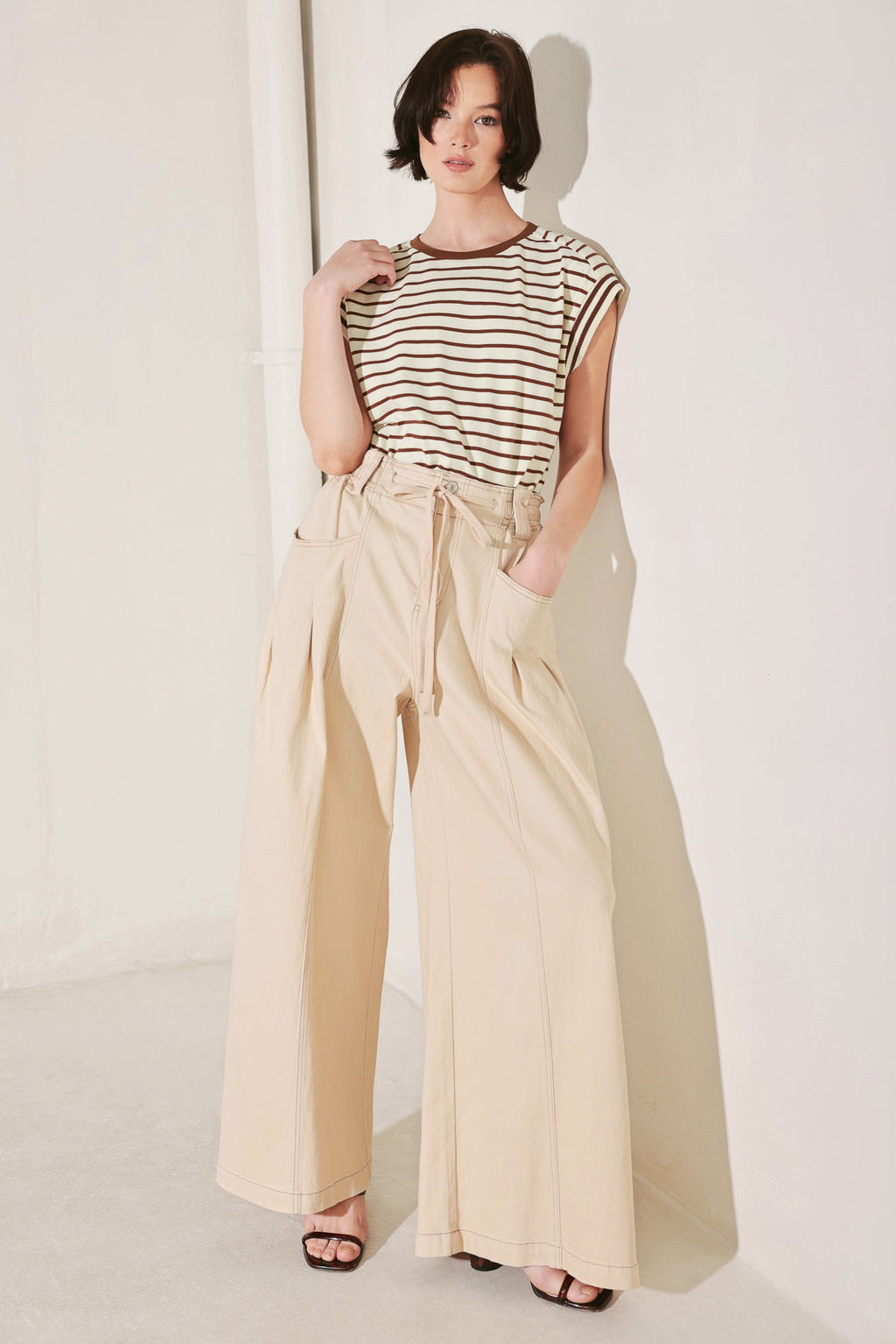 Woman wearing a striped top and beige wide-leg pants against a white background