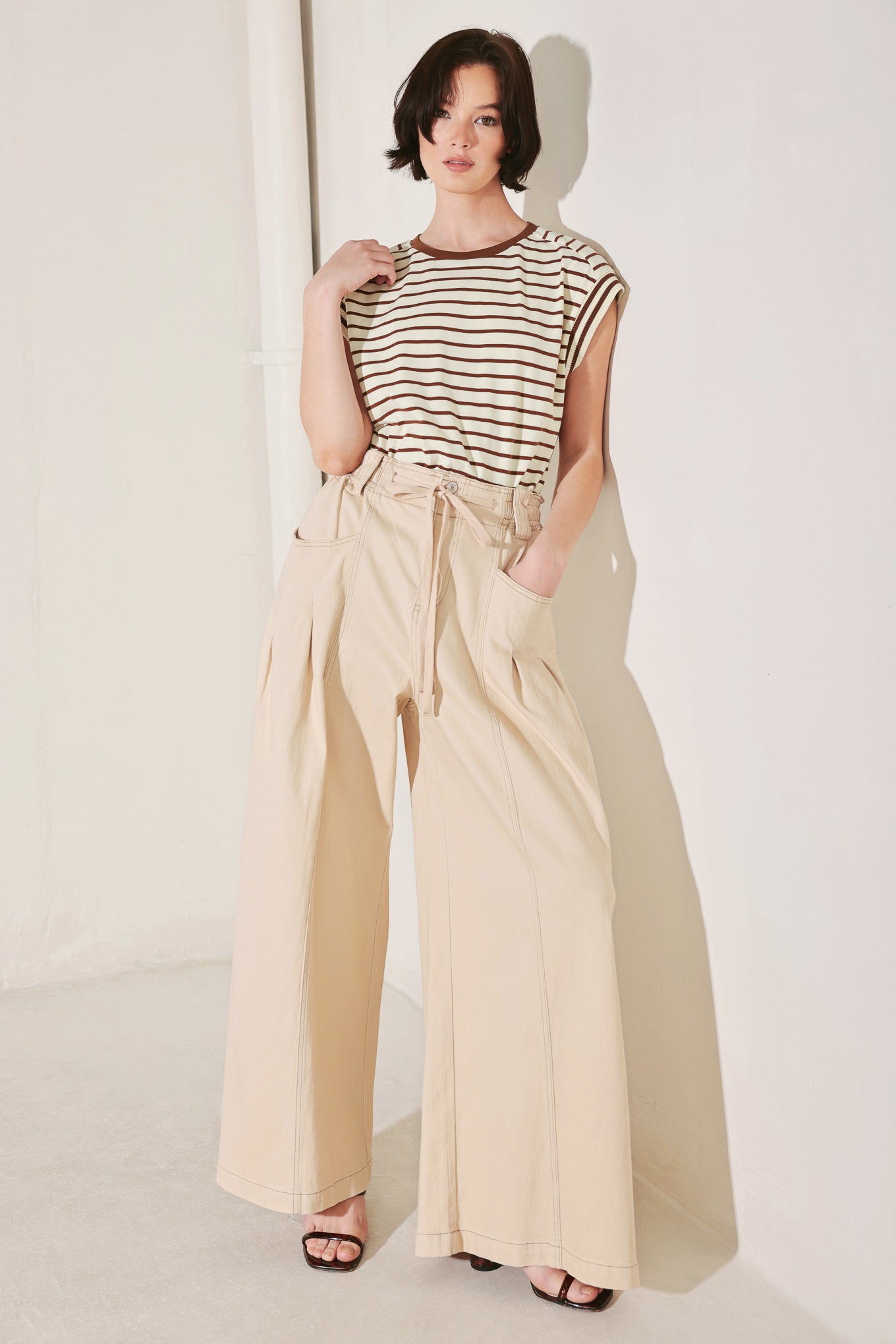 Woman wearing a striped top and beige wide-leg pants against a white background