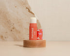 Two lip balm sticks on a wooden block with a pink tiled background