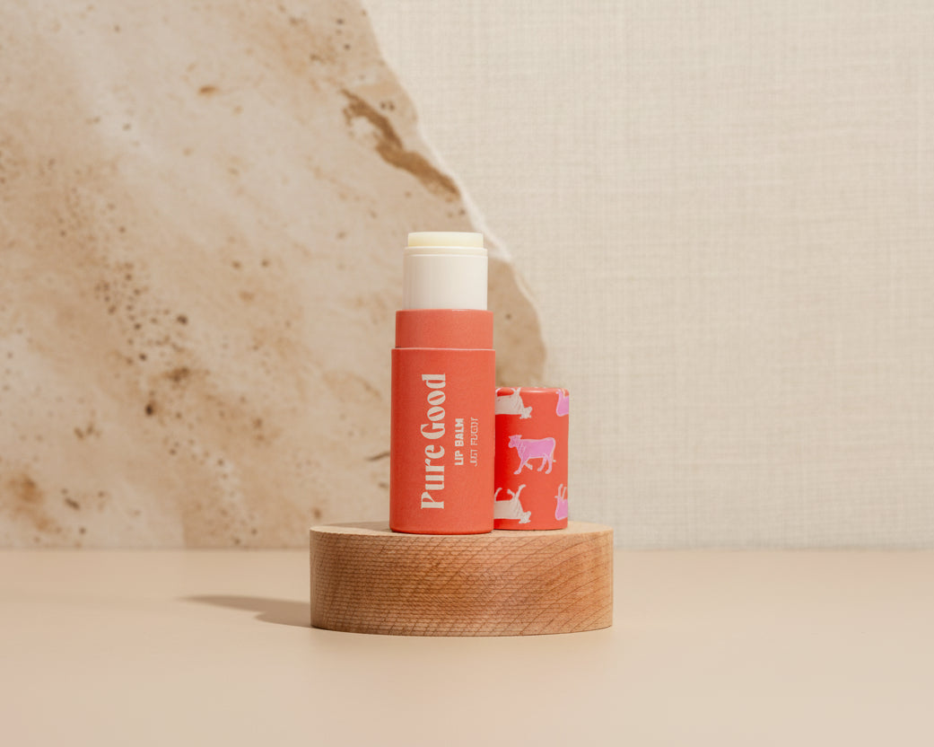 Two lip balm sticks on a wooden block with a pink tiled background