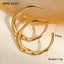 Gold hoop earrings on a textured beige surface with measurement details.