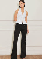Woman wearing a white halter top and black flared pants against a light wooden panel background
