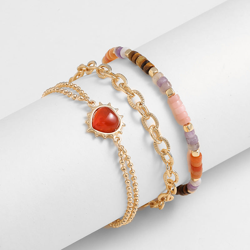 Set of three bracelets with gold chain, red stone, and beaded designs on a white surface