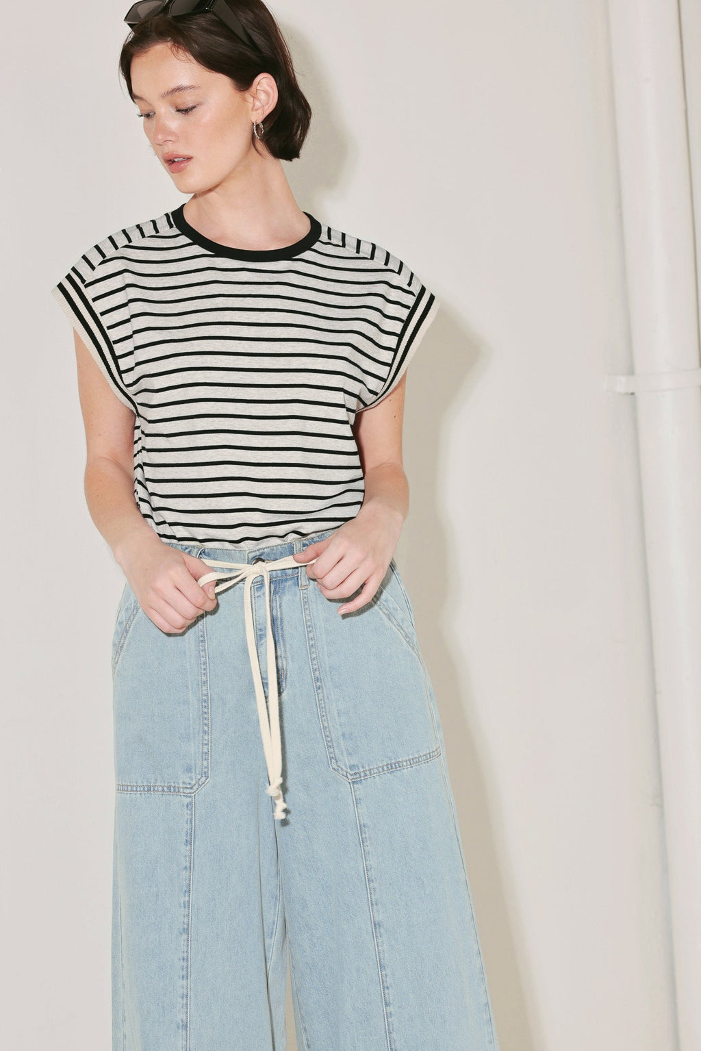 Person wearing a black and white striped top and light blue denim pants against a plain background
