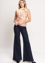 Woman wearing a sleeveless top with floral pattern and dark flared pants on a white background