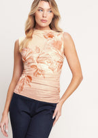 Woman wearing a sleeveless floral top and dark pants on a plain background
