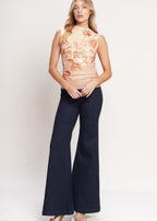 Woman wearing a floral top and dark blue flared pants on a white background