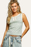 Woman wearing a patterned sleeveless top and jeans against a gray background