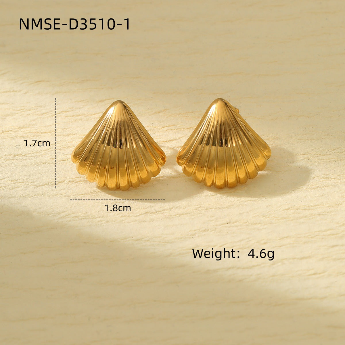 Gold shell-shaped earrings with measurements and weight on a light wood background