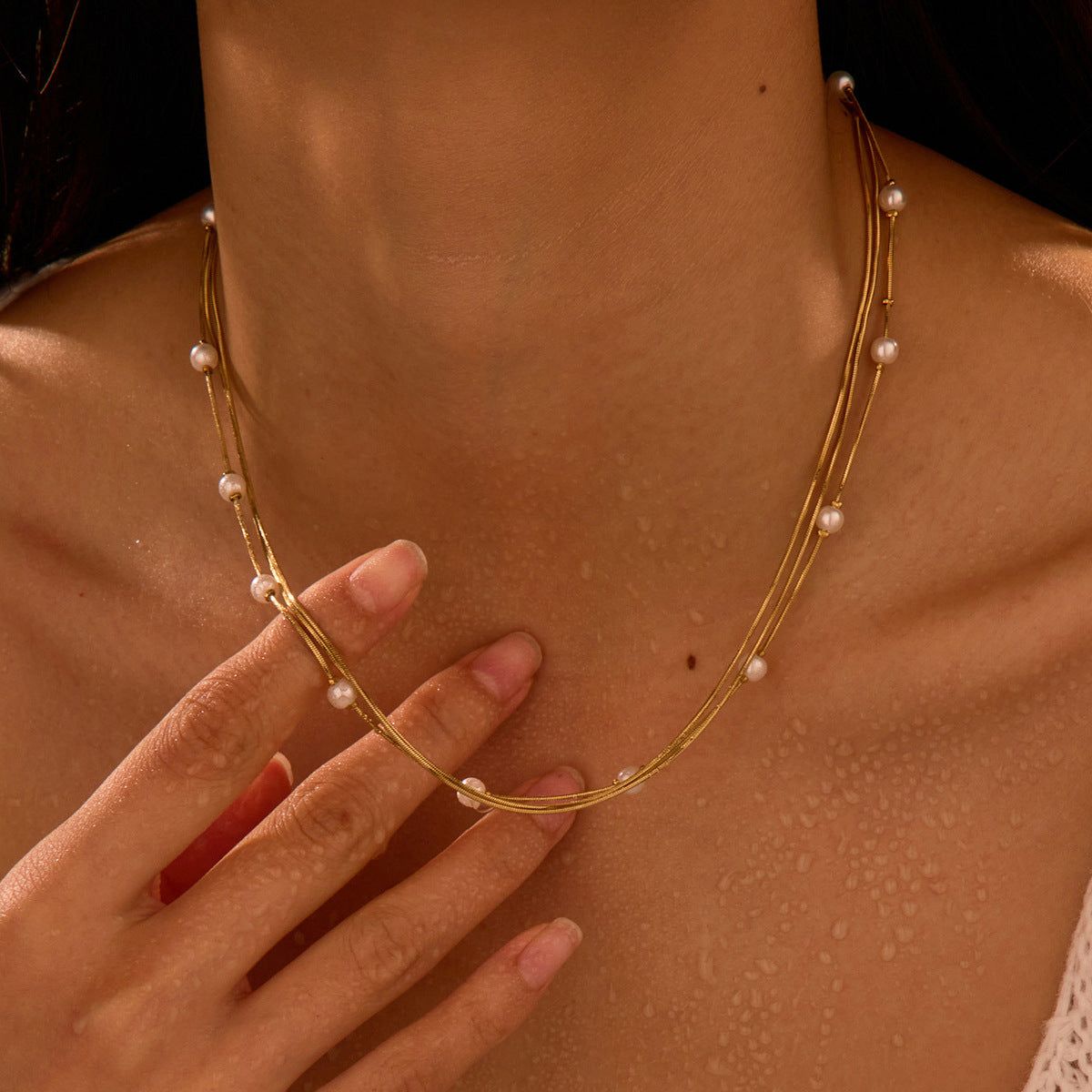 Gold necklace with pearls worn by a person, with a hand touching the neck. Main image