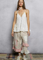 Woman wearing a white lace top and pants with pink accents against a gray background