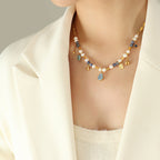 Necklace with pearls and gemstones worn by a person in a cream outfit