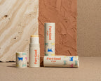 Four 'Pure Good' lip balm containers on a pink tiled background