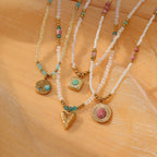 Three beaded necklaces with gold pendants on a beige fabric background