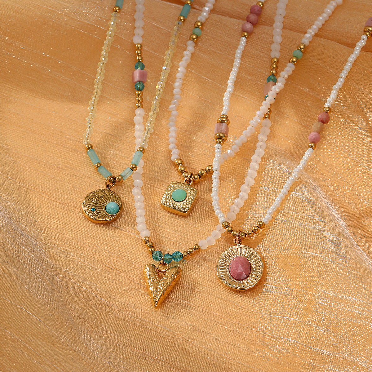 Three beaded necklaces with gold pendants on a beige fabric background