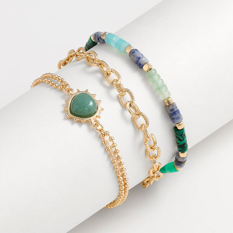 Set of three bracelets with gold chain, green stone, and beaded design on a white background