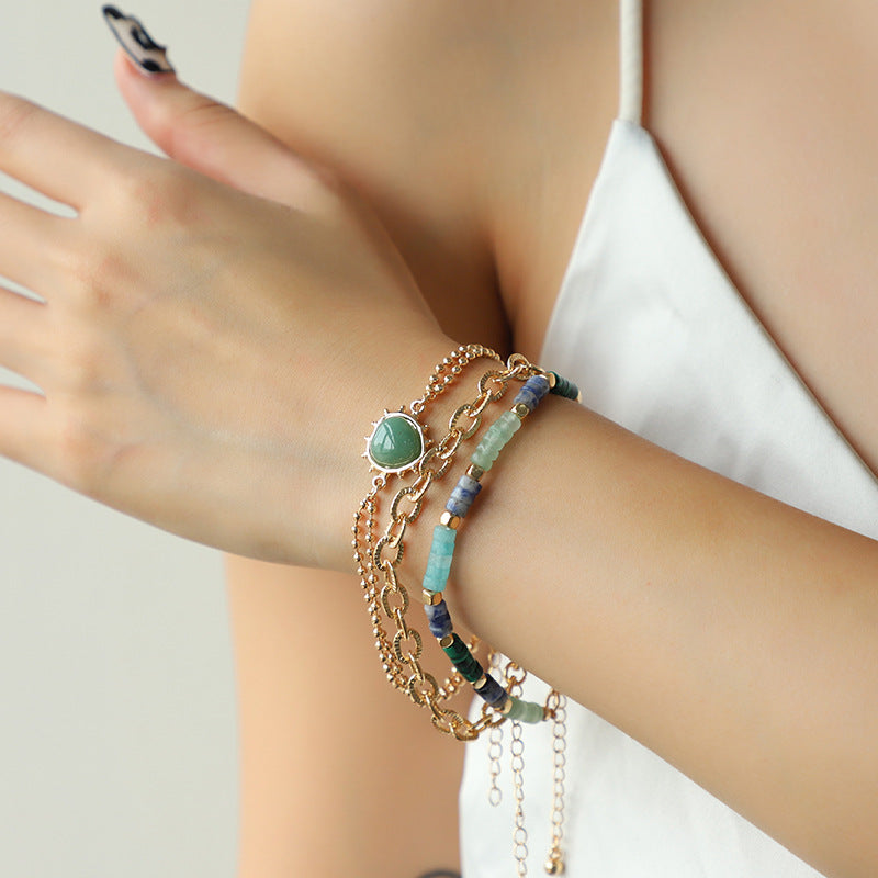 Close-up of a wrist wearing multiple bracelets with green and blue beads on a neutral background