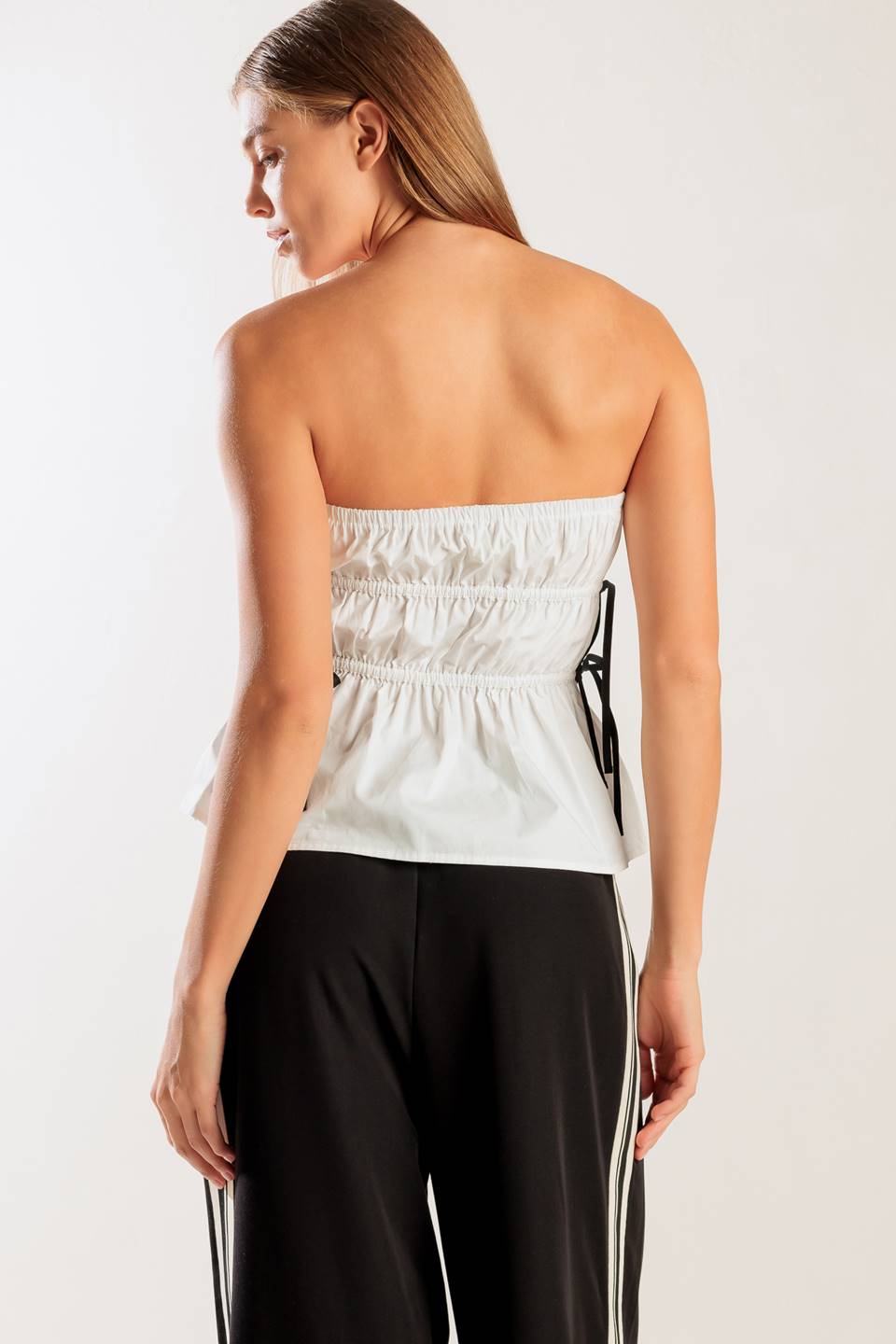 Woman wearing a strapless white top and black pants on a plain background