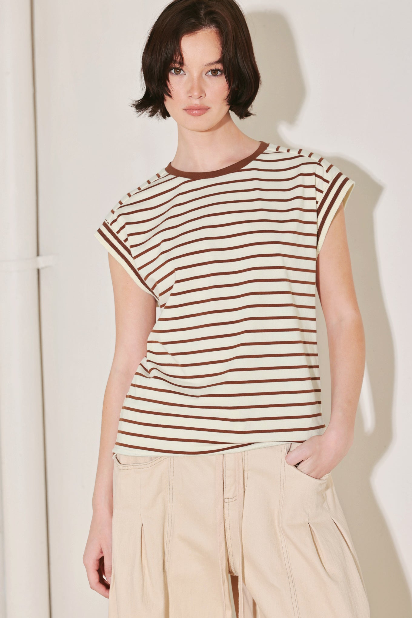 Woman wearing a striped shirt and beige pants against a plain background