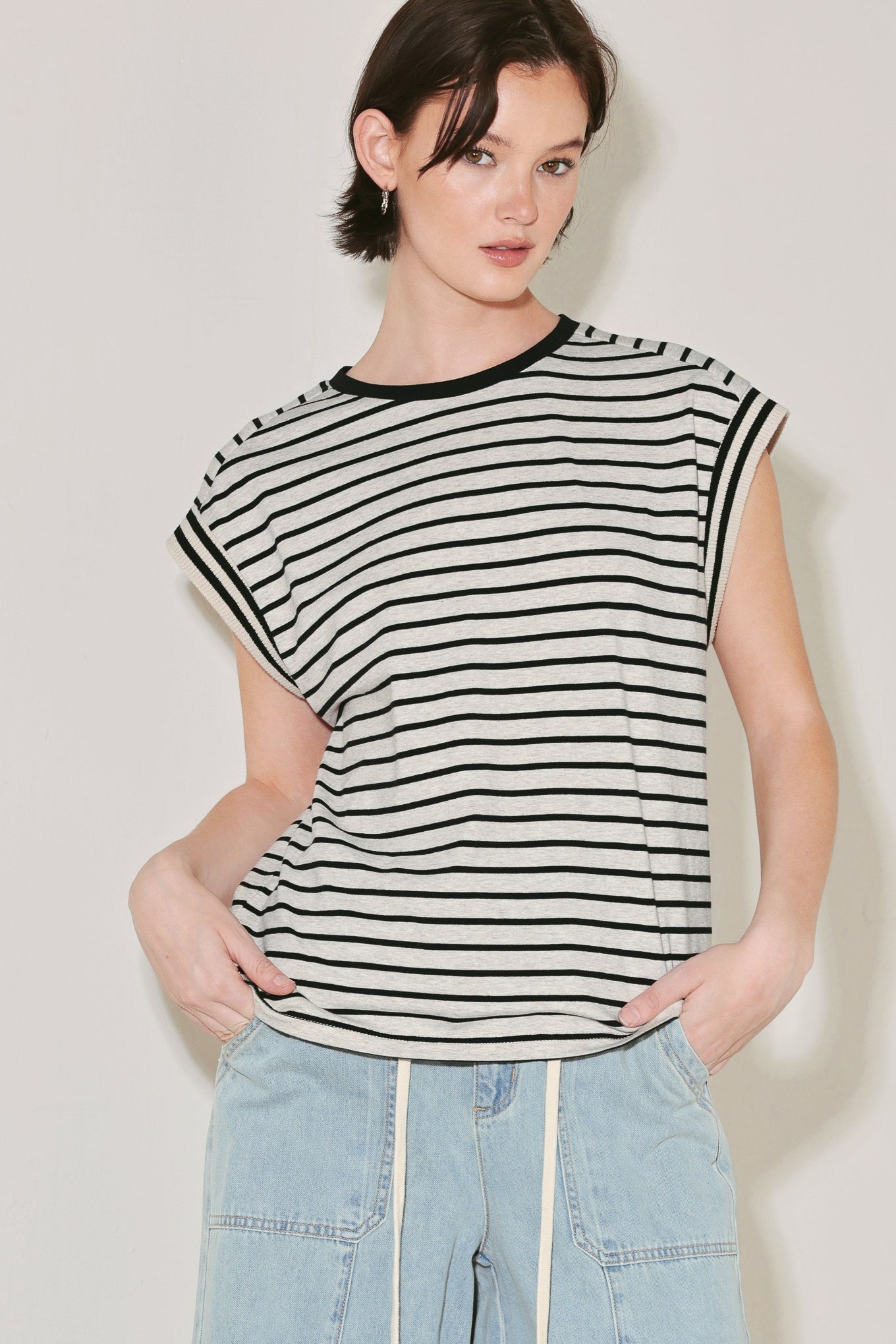 Woman wearing a black and white striped sleeveless top with light blue jeans against a plain background Main image