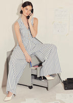 Woman in a striped jumpsuit sitting on a rolling chair, talking on a phone in an office setting.