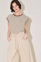 Woman wearing a striped sleeveless top and beige pants against a plain background