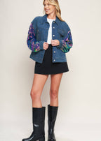Women wearing statement denim jacket with multicolor sequin sleeves styled with black skirt and boots