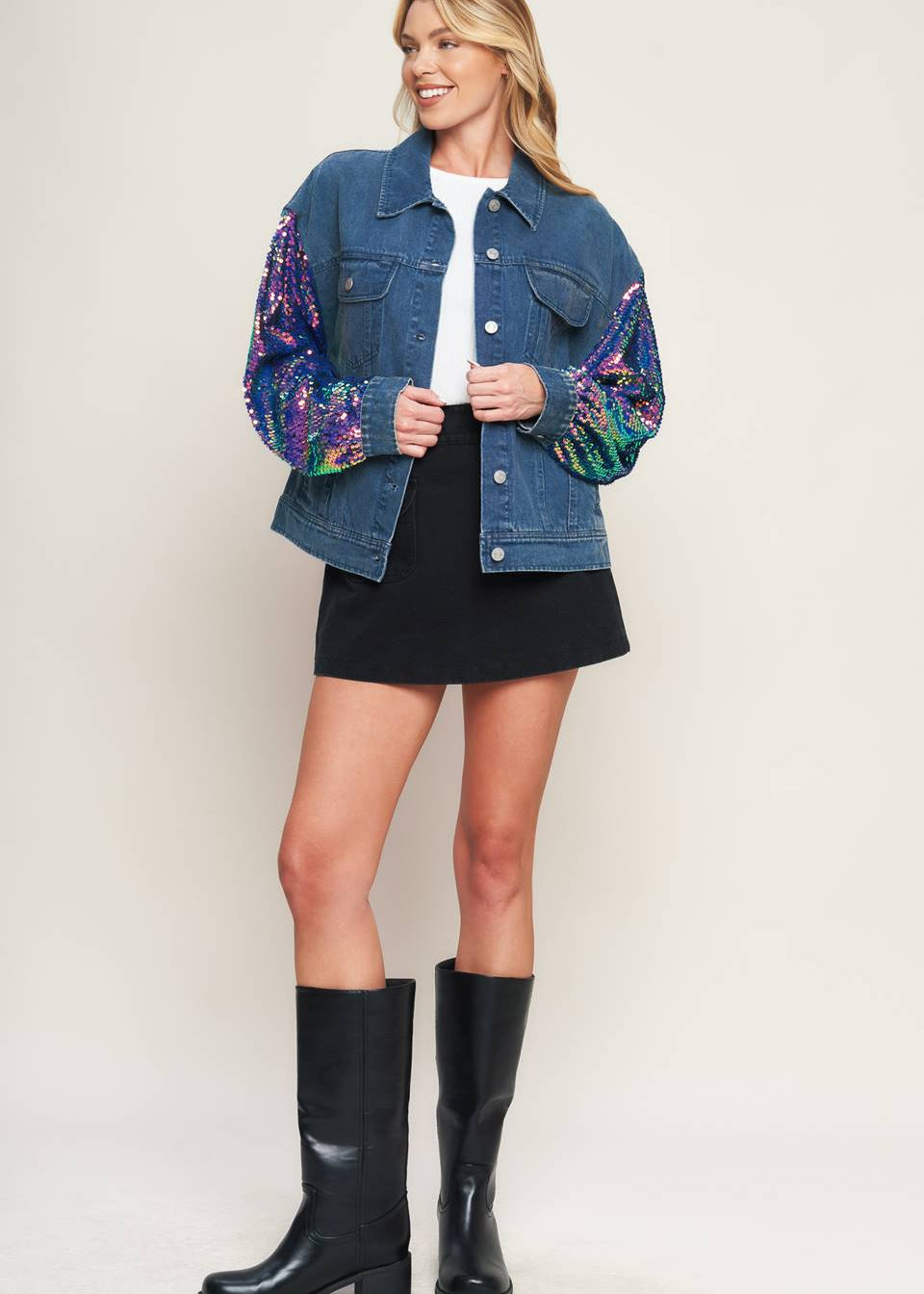 Women wearing statement denim jacket with multicolor sequin sleeves styled with black skirt and boots
