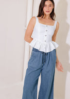 Woman wearing a white peplum top and blue pants against a plain background
