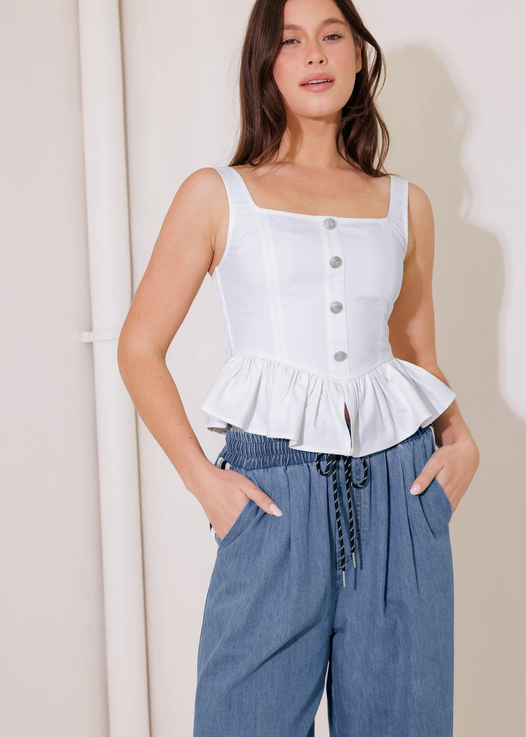 Woman wearing a white peplum top and blue pants against a plain background