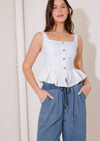 Woman wearing a white peplum top and blue pants against a plain background