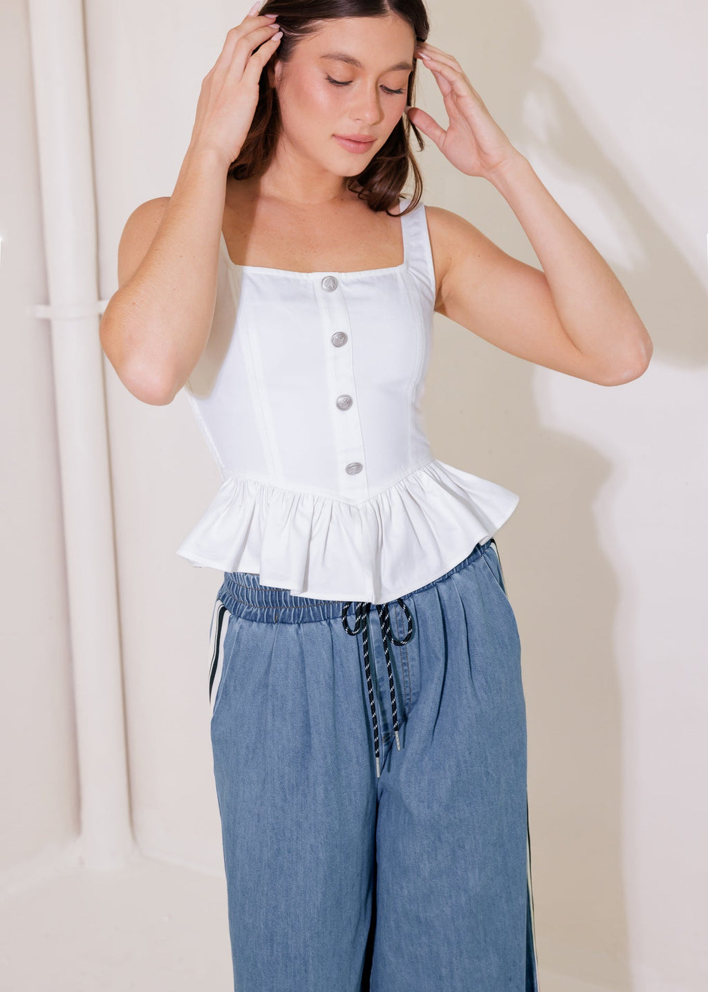Woman wearing a white peplum top and blue pants against a plain background