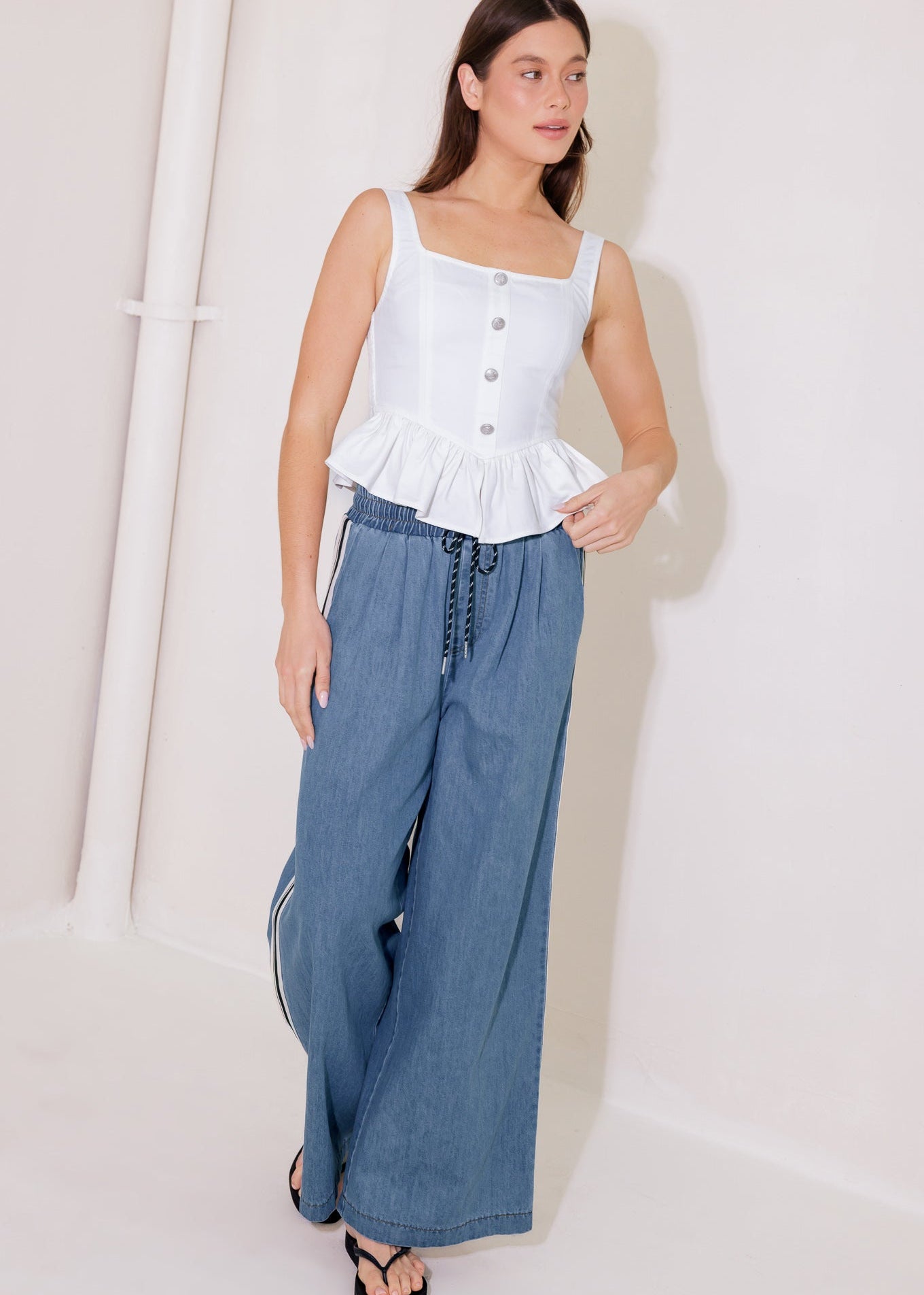 Woman wearing a white top with a peplum waist and blue wide-leg pants against a white background